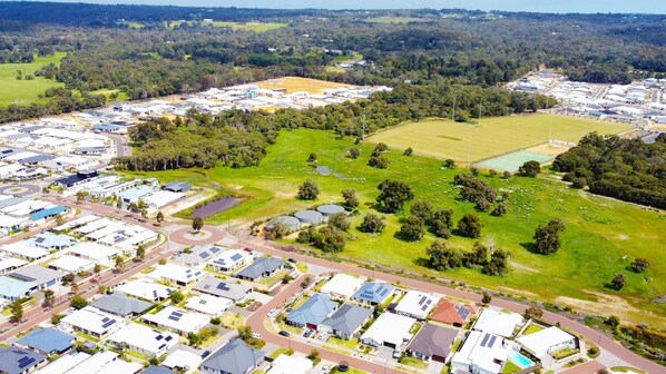 An aerial view of a residential area with multiple houses, a central green space, and a sports field.