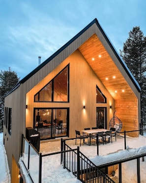 A modern wooden cabin with a large dining area and a covered outdoor seating space.