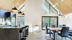 A modern kitchen with a central island, bar stools, and a dining area with a large table and chairs. - Chalet OSLO | Design & forest | Spa - Silence (Saint-Cã´Me)