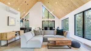 A modern living room with a large sectional sofa, a wooden coffee table, and a dining area with a kitchen in the background. - Chalet OSLO | Design & forest | Spa - Silence (Saint-Cã´Me)