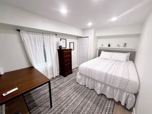A bedroom with a bed, a dresser, a desk, and a window with curtains.