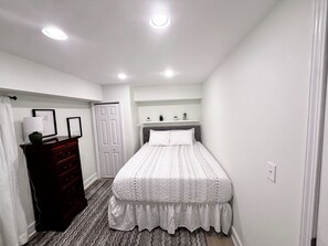 Une chambre à coucher avec un lit, une commode et une petite étagère avec des plantes.