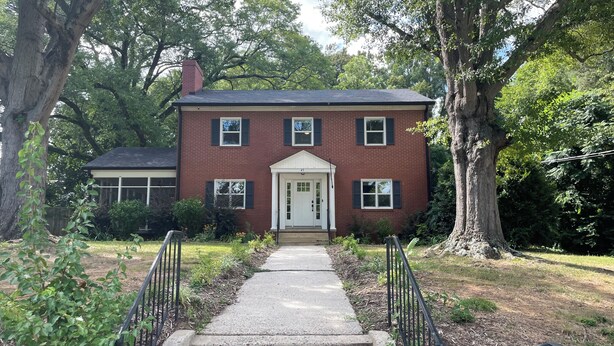 A two-story brick house with a front entrance, a small porch, and a pathway leading to the door.