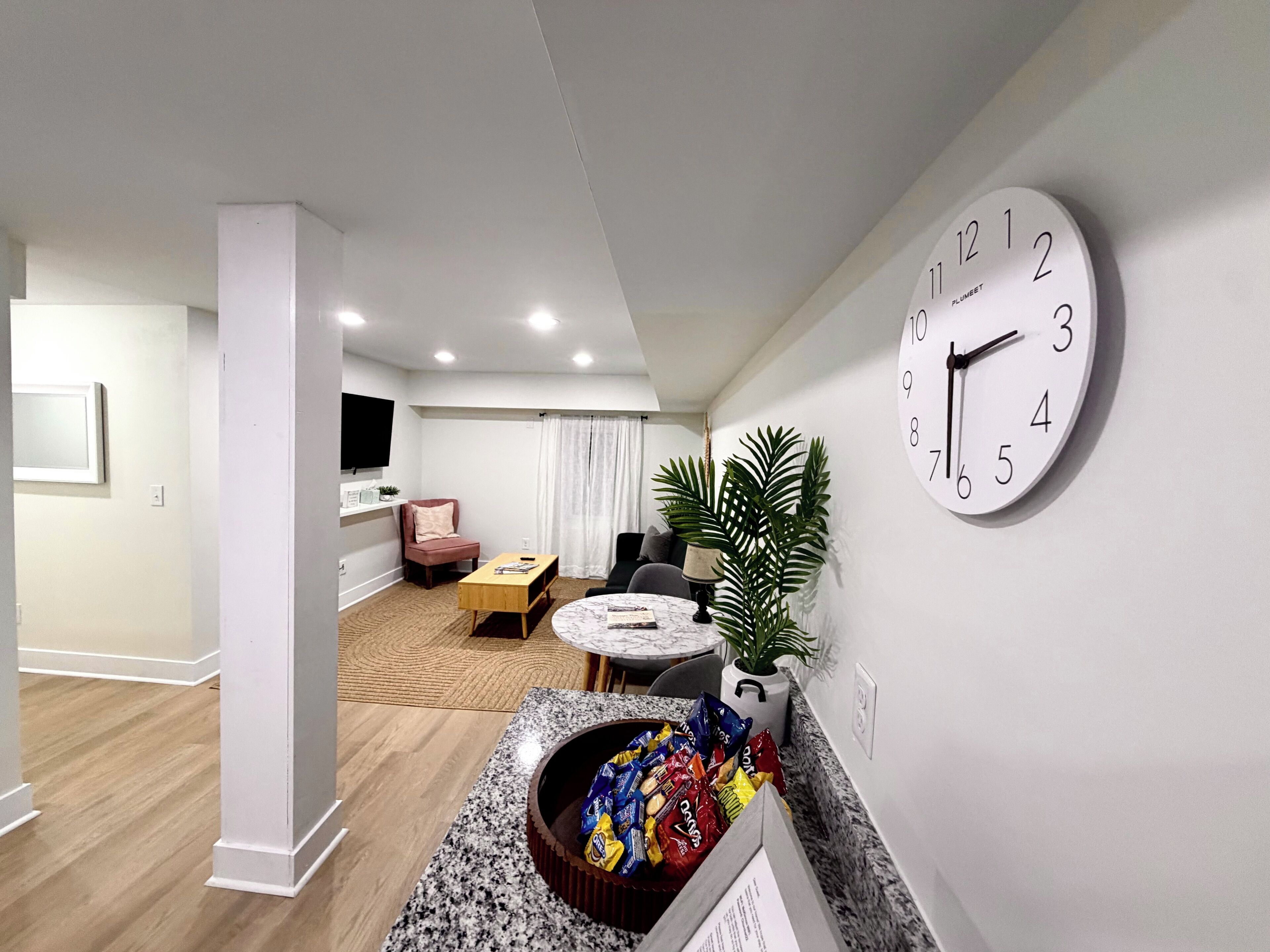 Una sala de estar moderna con una mesa de centro redonda, un sofá cómodo, un televisor montado en la pared y un reloj de pared grande.