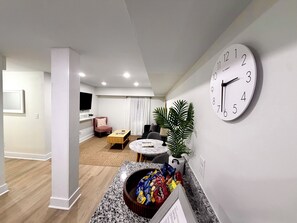 Un salon moderne avec une table basse ronde, un canapé confortable, un téléviseur fixé au mur et une grande horloge murale.