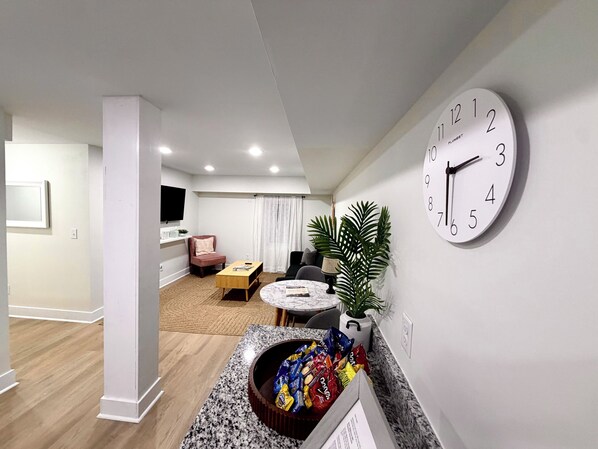 A modern living room with a round coffee table, a comfortable sofa, a TV mounted on the wall, and a large wall clock.