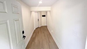 A hallway with white walls and wooden flooring, leading to a door with a sign above it.