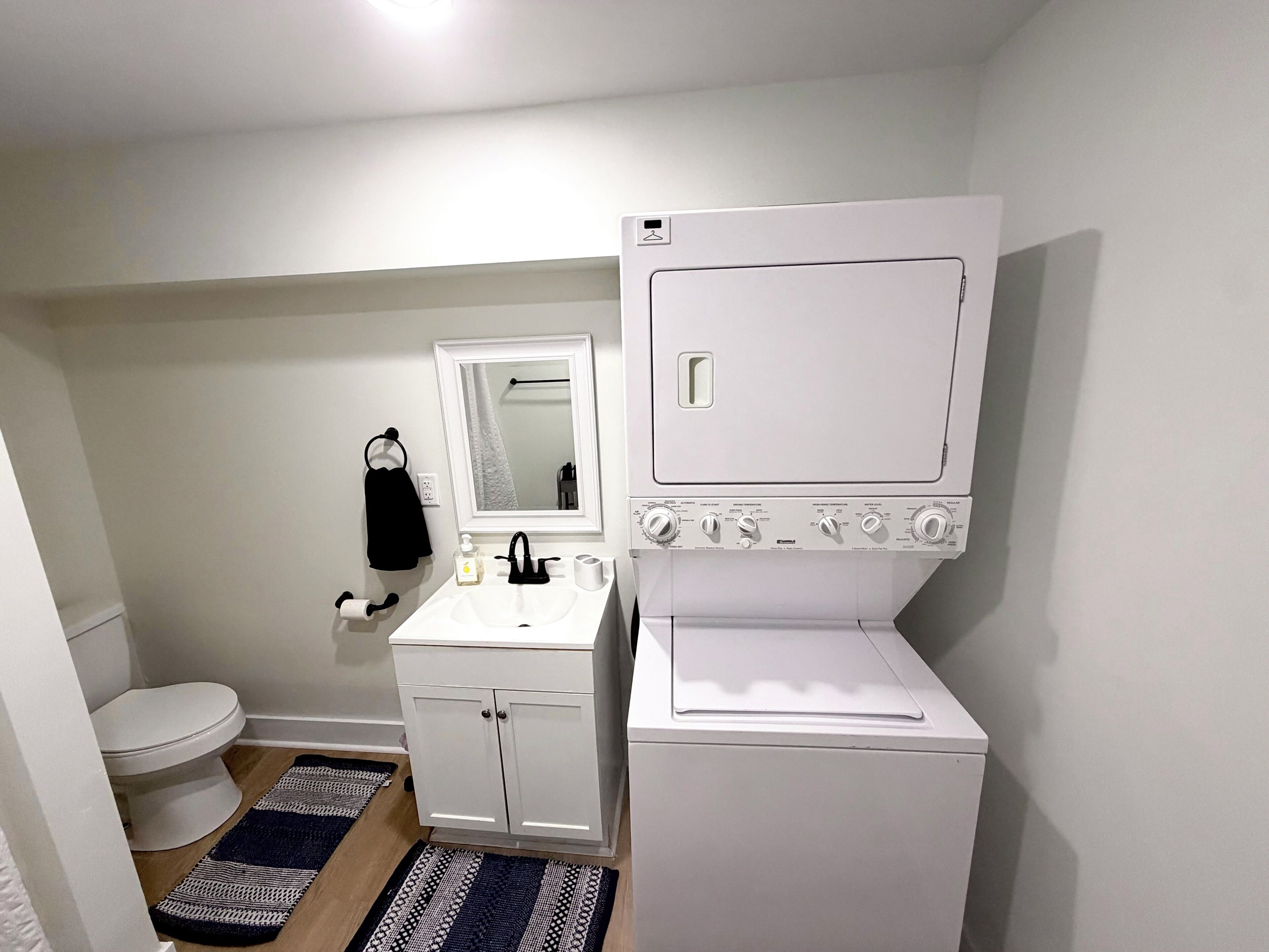 A compact bathroom with a toilet, sink, mirror, and a white washing machine.