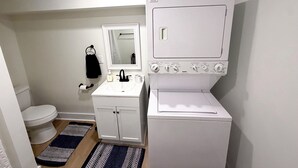 A compact bathroom with a toilet, sink, mirror, and a white washing machine.