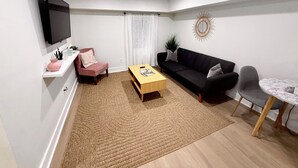 A modern living room with a flat-screen TV, a sofa, a coffee table, a chair, and a small dining table.
