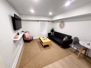 Een moderne woonkamer met een flatscreen televisie, een bank, een salontafel, een stoel en een eettafel.