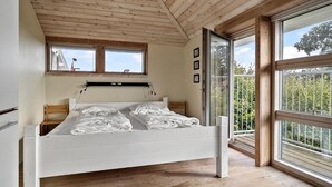 Camera da letto con soffitto in legno, un letto, una finestra e vista su piante.