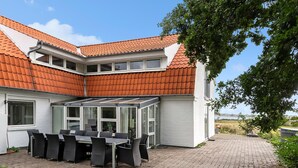 Una casa con tetto spiovente, veranda in vetro con mobili da esterno e vialetto in pietra.