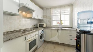 A kitchen with white cabinets, a microwave, a stove, an oven, a washing machine, and a water dispenser. - Beatifull Apartam 14A 2 Bedroom Sea Medano (Granadilla de Abona)