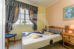 A bedroom with a bed, a chair, a nightstand, and a window with curtains. - Beatifull Apartam 14A 2 Bedroom Sea Medano (Granadilla de Abona)