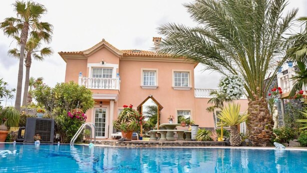 A pool area with a large building in the background, palm trees, and various plants. - Beatifull Apartam 14A 2 Bedroom Sea Medano (Granadilla de Abona)