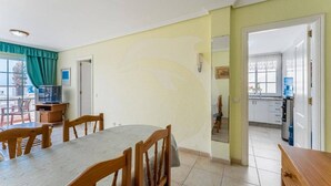 A dining area with a round table and chairs, a television, and a kitchen visible through an open doorway. - Beatifull Apartam 14A 2 Bedroom Sea Medano (Granadilla de Abona)