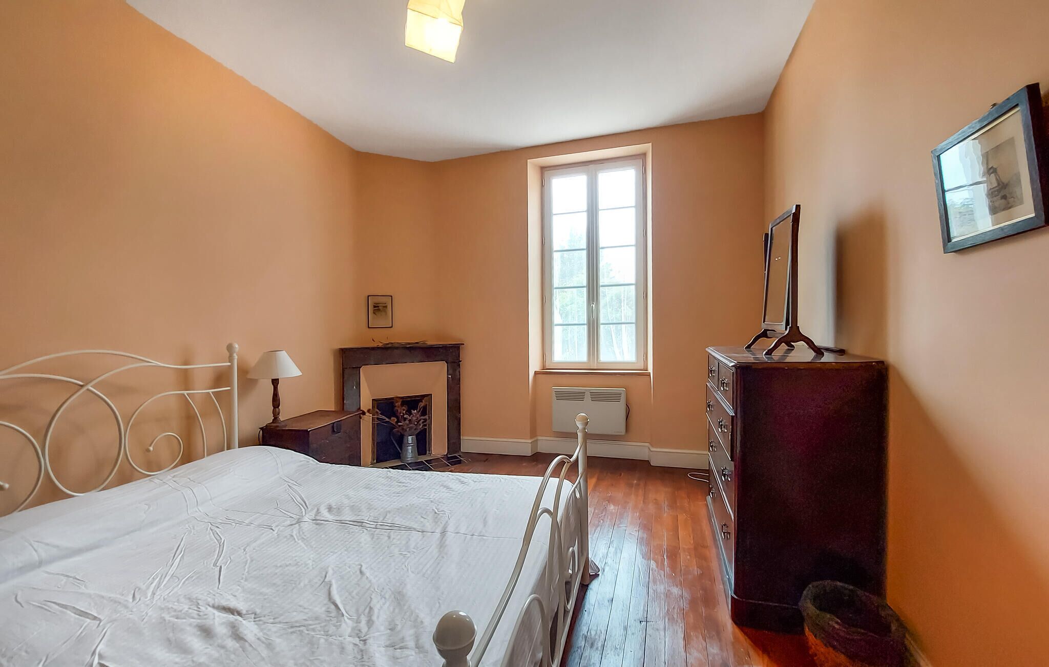 Une chambre à coucher avec un lit, une commode, une fenêtre et une cheminée.