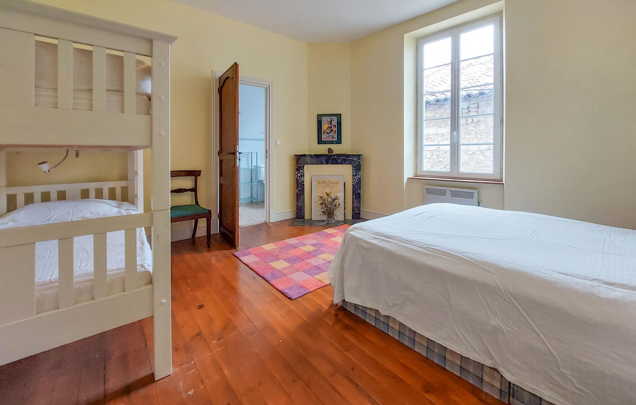 A bedroom with a bunk bed, a single bed, a fireplace, and a window.