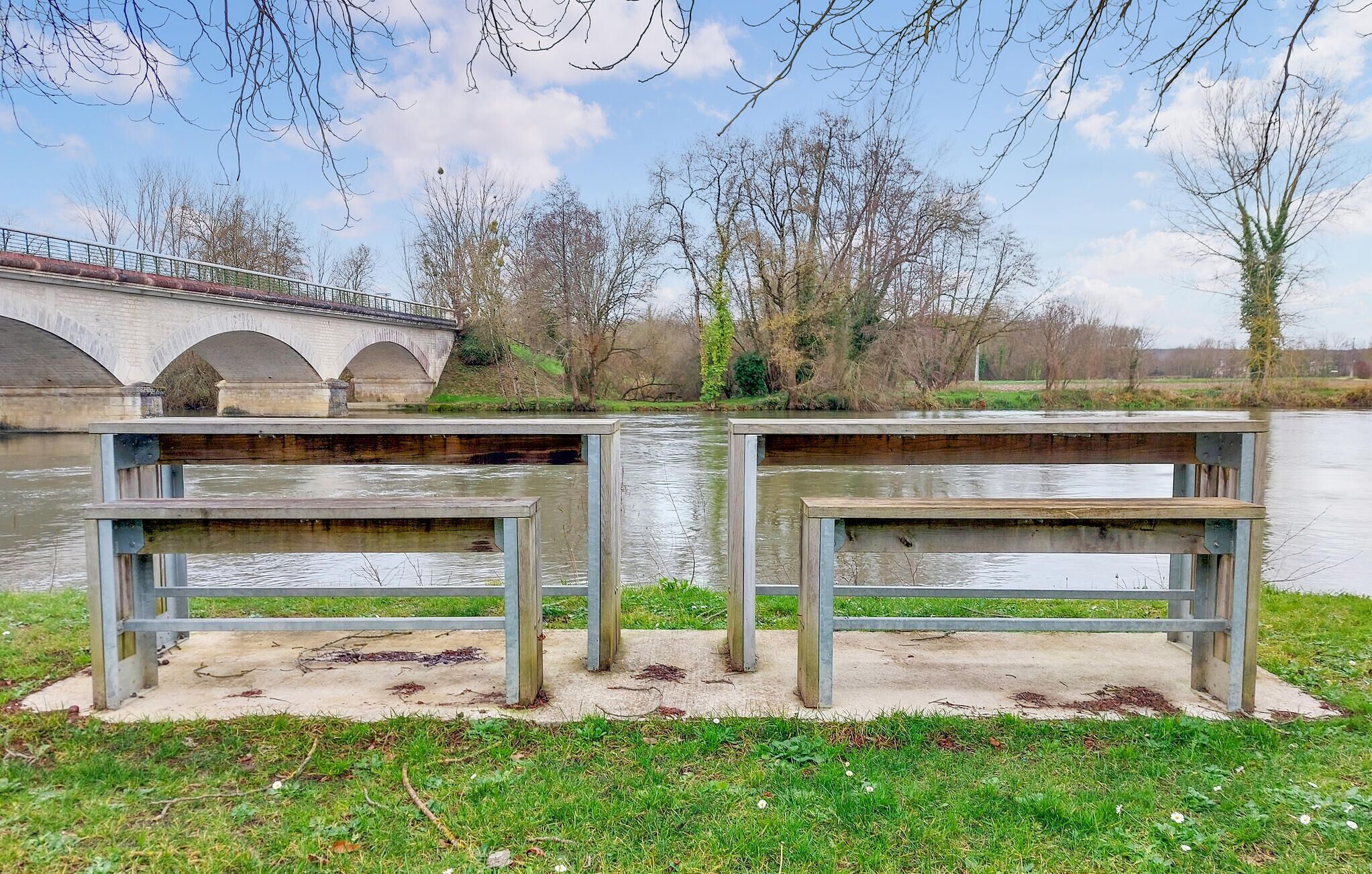 A riverside bench area with a bridge in the background.