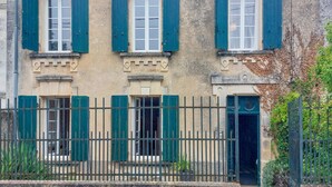 Un bâtiment doté de trois fenêtres, chacune ornée de volets verts, et d’une clôture en métal noir à l’avant.