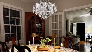 A dining area with a chandelier, wooden chairs, a floral tablecloth, and a wooden cabinet with glass doors. - Stay on Magnolia Hill 3BR Cottage in Meridian, Mississippi with Southern Charm (Meridian)