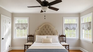 A bedroom with a large bed, two chairs, a ceiling fan, and two windows with curtains. - Stay on Magnolia Hill 3BR Cottage in Meridian, Mississippi with Southern Charm (Meridian)