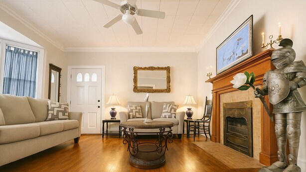 A living room with a wooden floor, a sofa, a round coffee table, a fireplace with a statue, and a ceiling fan. - Stay on Magnolia Hill 3BR Cottage in Meridian, Mississippi with Southern Charm (Meridian)