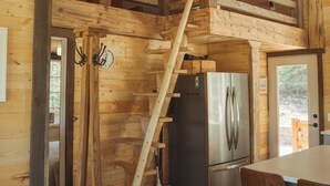 A wooden cabin interior with a wooden staircase, a stainless steel refrigerator, and a dining area with wooden chairs.