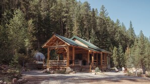 A wooden cabin with a porch, surrounded by a forest.