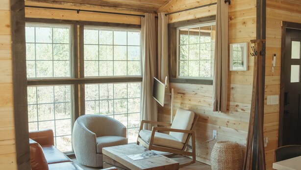 A cozy cabin interior with a wooden interior, large windows, a sofa, a chair, and a television.