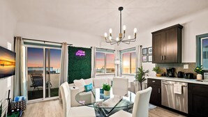Una cocina moderna con una mesa de comedor de vidrio, armarios oscuros y vistas al atardecer a través de amplias ventanas.