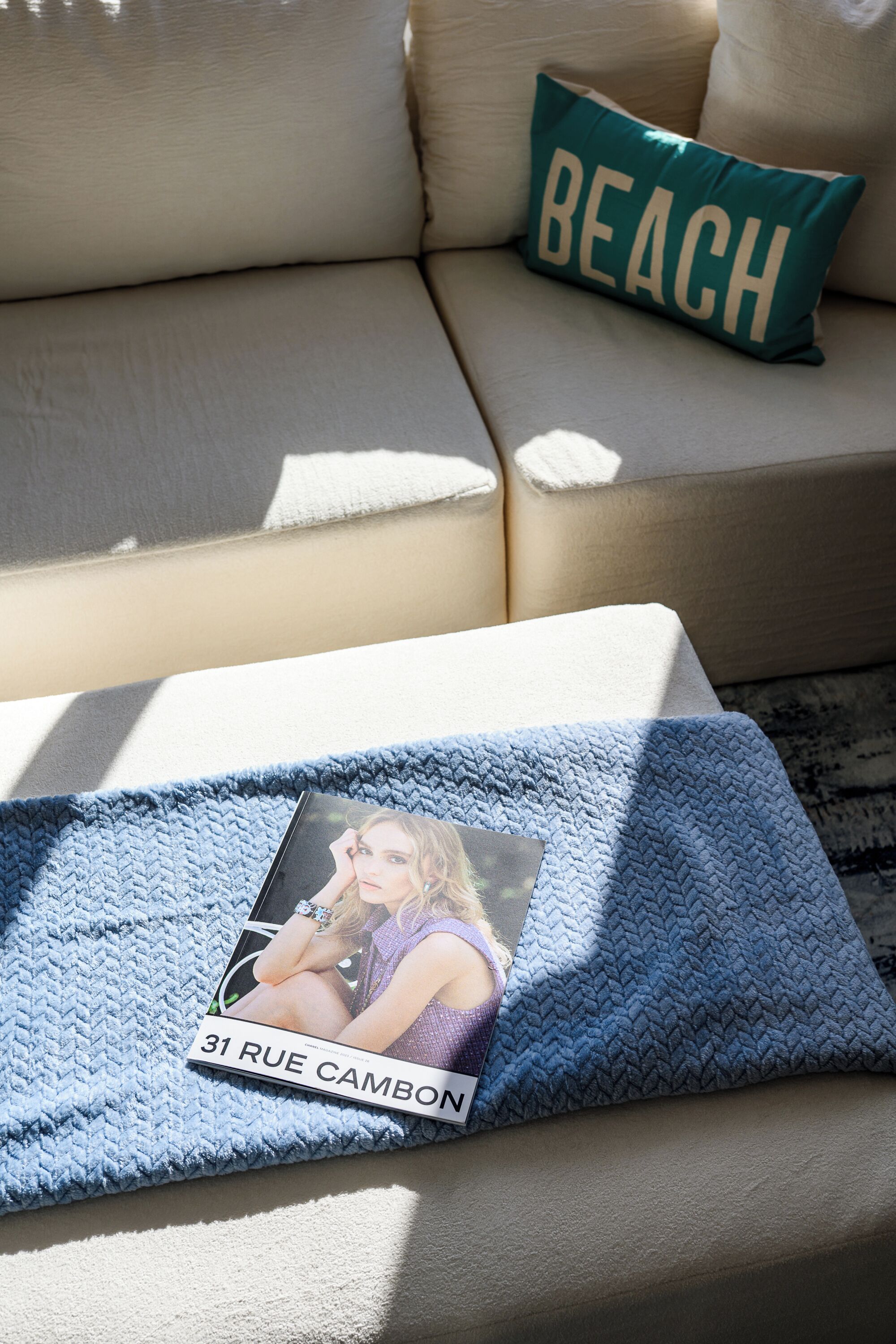 A sofa with a cushion labeled "BEACH" and a blanket with a photo and address "31 RUE CAMBON".