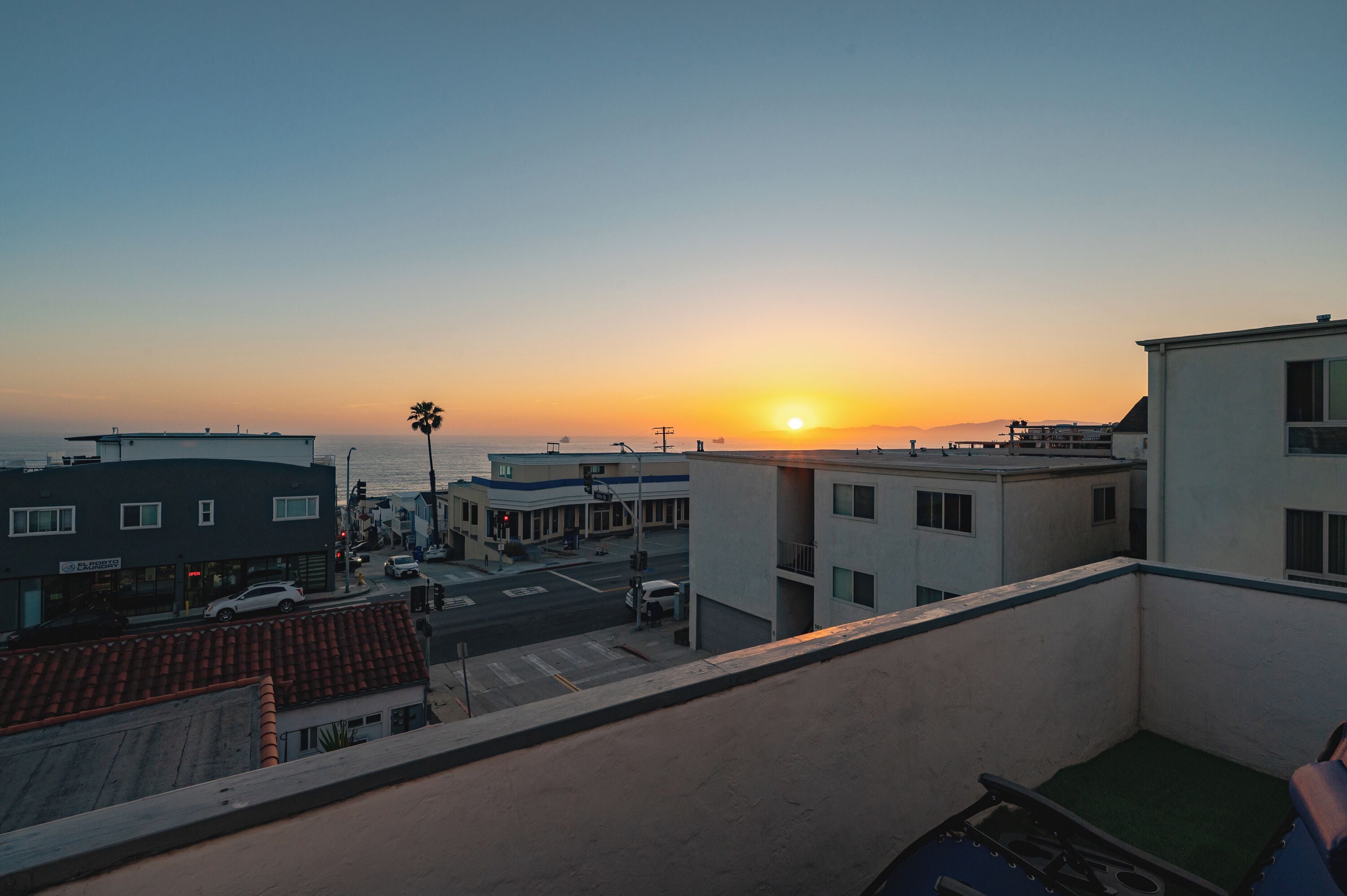 A sunset view from a balcony overlooking a street with buildings and a palm tree.
