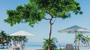 Une terrasse donnant sur la plage, agrémentée d’un arbre, de parasols blancs et de chaises.