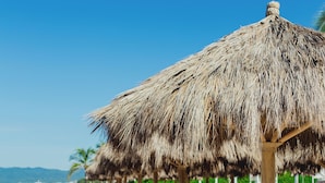 Une plage avec des parasols en chaume et des palmiers.