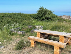 Una mesa de picnic de madera con bancos en un área verde con vista al mar.