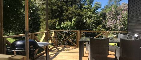 Una terraza de madera con mobiliario exterior, una parrilla y una bicicleta.