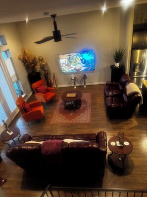 A modern living room with a flat-screen TV, leather sofas, a coffee table, and a ceiling fan.