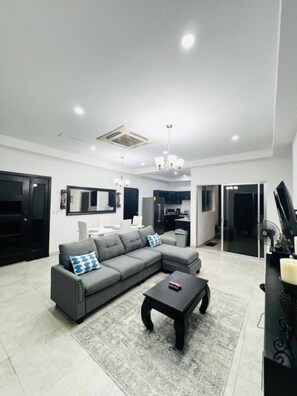 A modern living room with a grey sectional sofa, a black coffee table, and a patterned rug.
