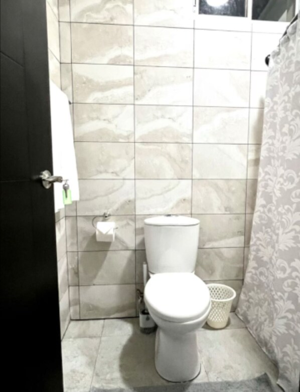 A bathroom with a toilet, a towel hanging on the wall, and a shower curtain.