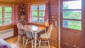 A wooden cabin interior with a dining table and four chairs, a window with a curtain, and a door with a view of greenery outside. - Awesome home in Hasle with house sea view (Hasle)