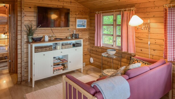 A cozy cabin interior with a wooden interior, a sofa, a small dining table, and a TV mounted on the wall. - Awesome home in Hasle with house sea view (Hasle)