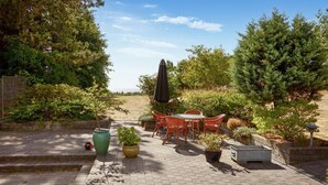 En terrasse med et bord og stole, omgivet af krukker med planter og træer.