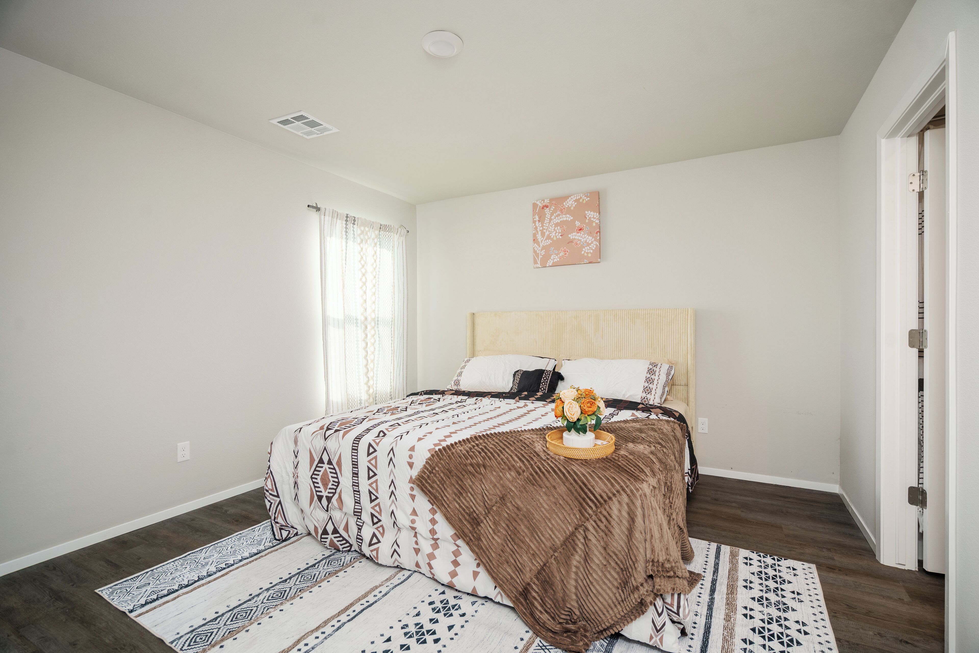 Quarto com cama, janela com cortinas, uma obra de arte na parede e porta.