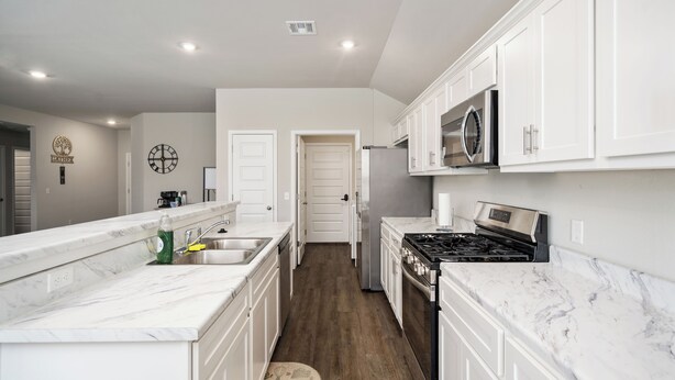 Una cocina moderna con armarios blancos, encimera de mármol, estufa y refrigerador.