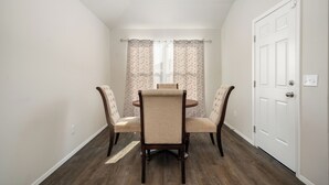 Un comedor con una mesa redonda y cuatro sillas, una puerta blanca y una ventana con cortinas traslúcidas.