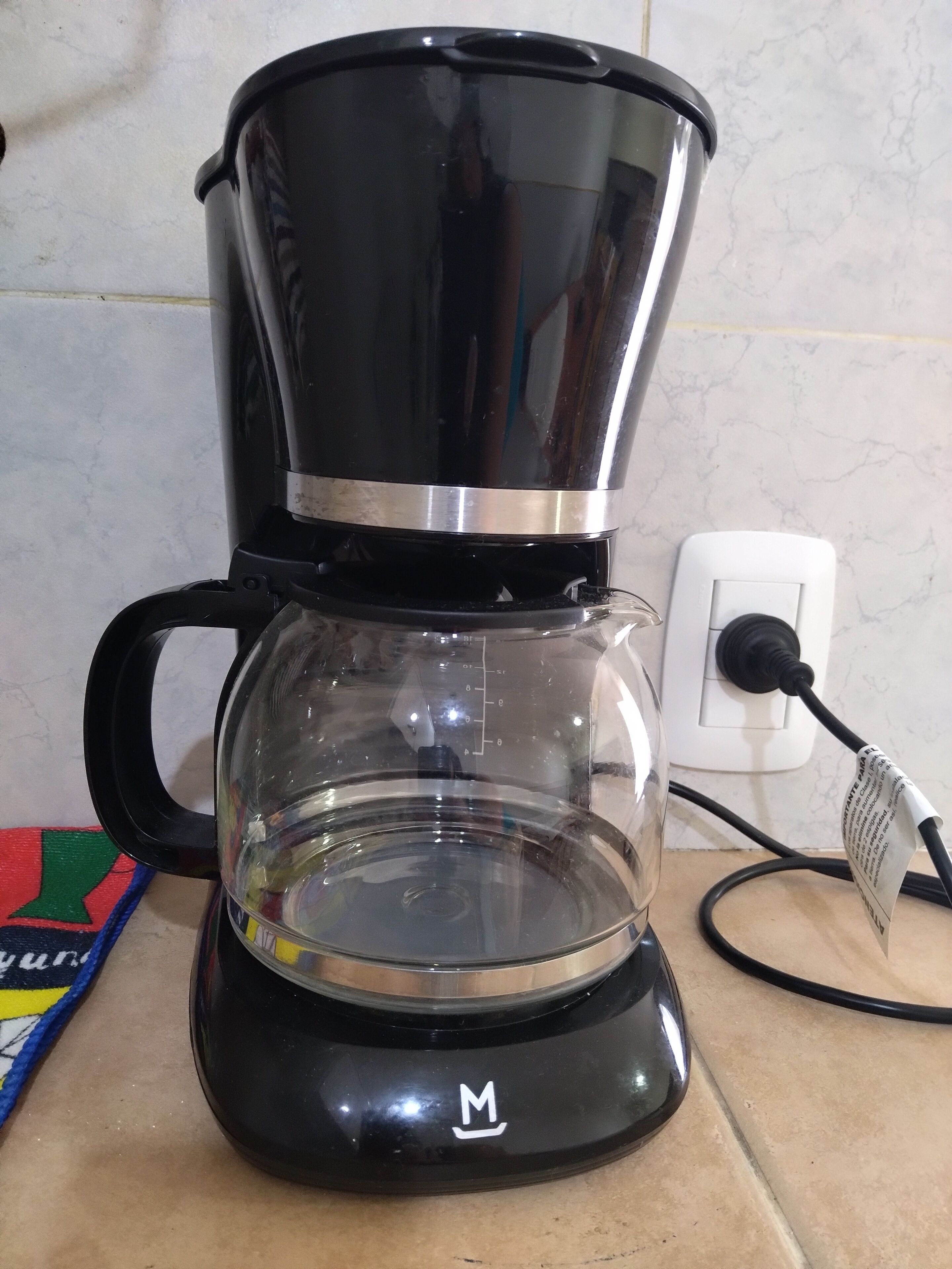 A black coffee maker with a clear glass carafe on a kitchen counter.