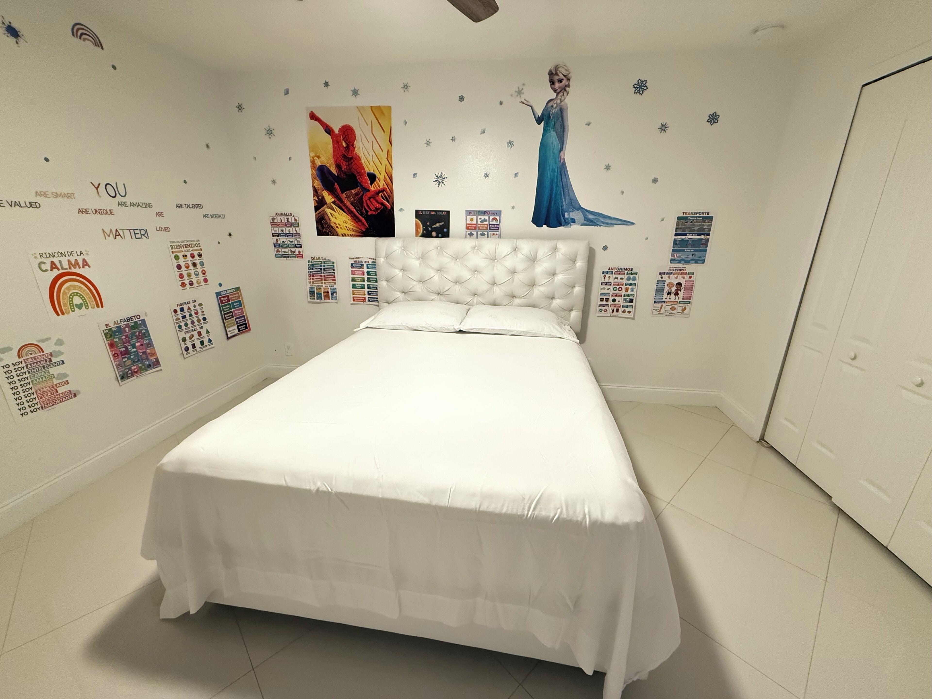 A bedroom with a white bed, a tufted headboard, and various motivational posters on the walls.