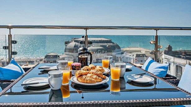A breakfast table with croissants, orange juice, and coffee, overlooking a coastal cityscape. - Penthouse on the Seafront (Worthing)